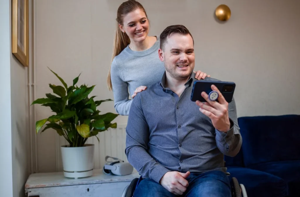 Disabled man in wheelchair with partner both looking at mobile phone and smiling